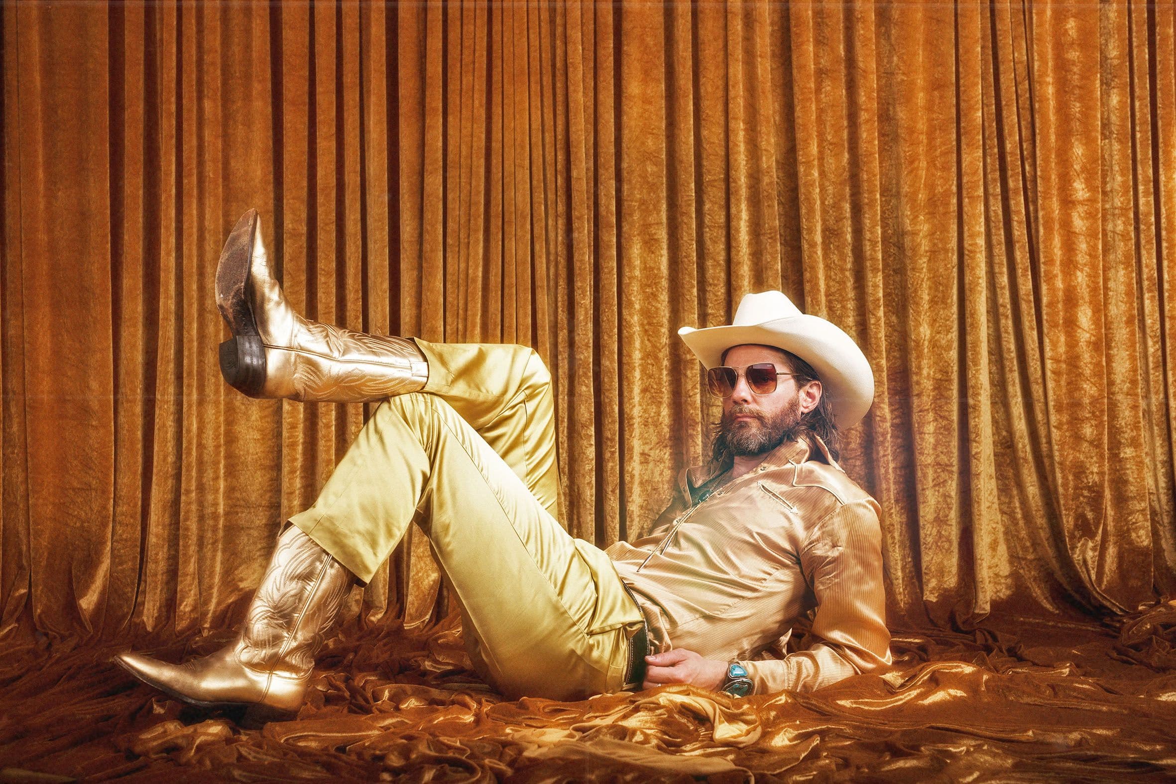 A man in a gold suit and cowboy boots on the floor.