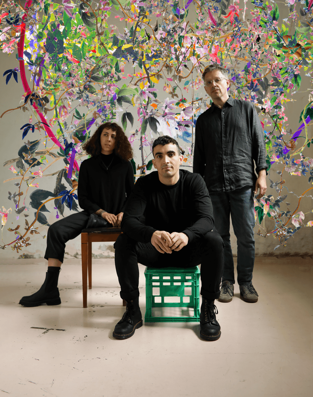 Three people sitting on a chair in front of a colorful wall.